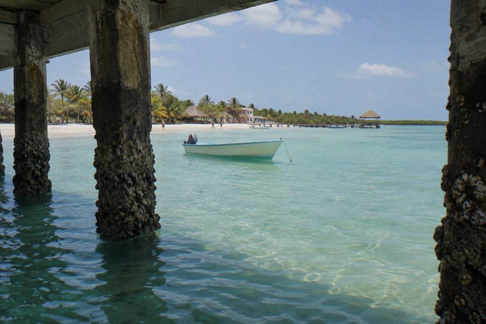 A small boat anchored in clear turquoise water near a sandy shoreline