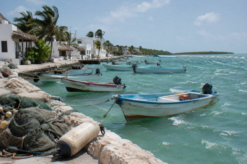 Colourful fishing boats tied along a seawall beside white buildings on a small island street