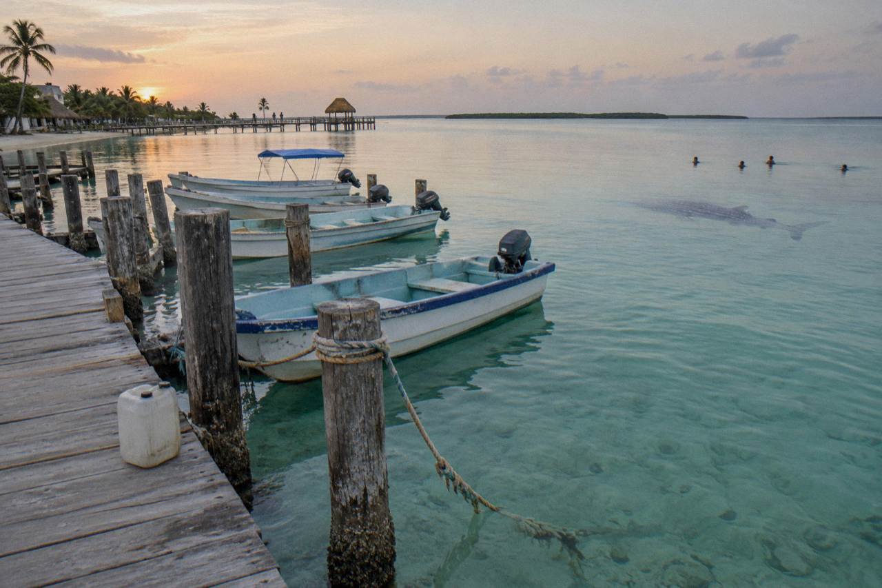 Wooden boats moored beside a shallow turquoise sea at a small island dock at dawn