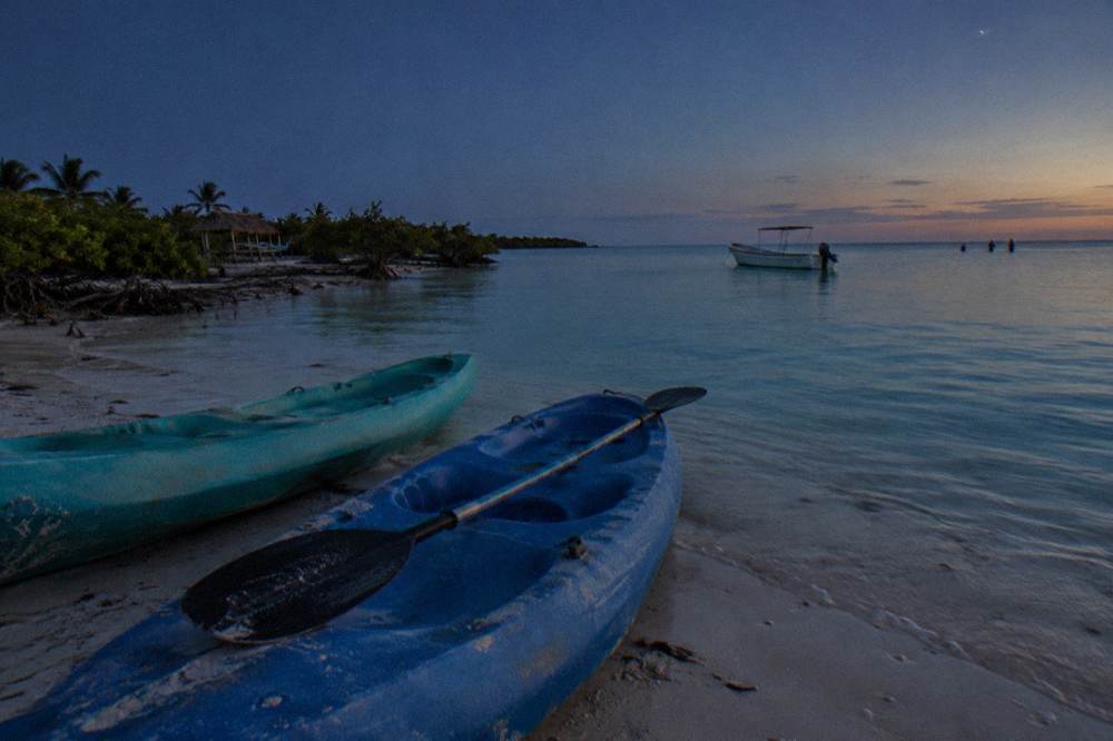 Kayaks resting on a calm shallow beach at dusk under a darkening sky with faint stars