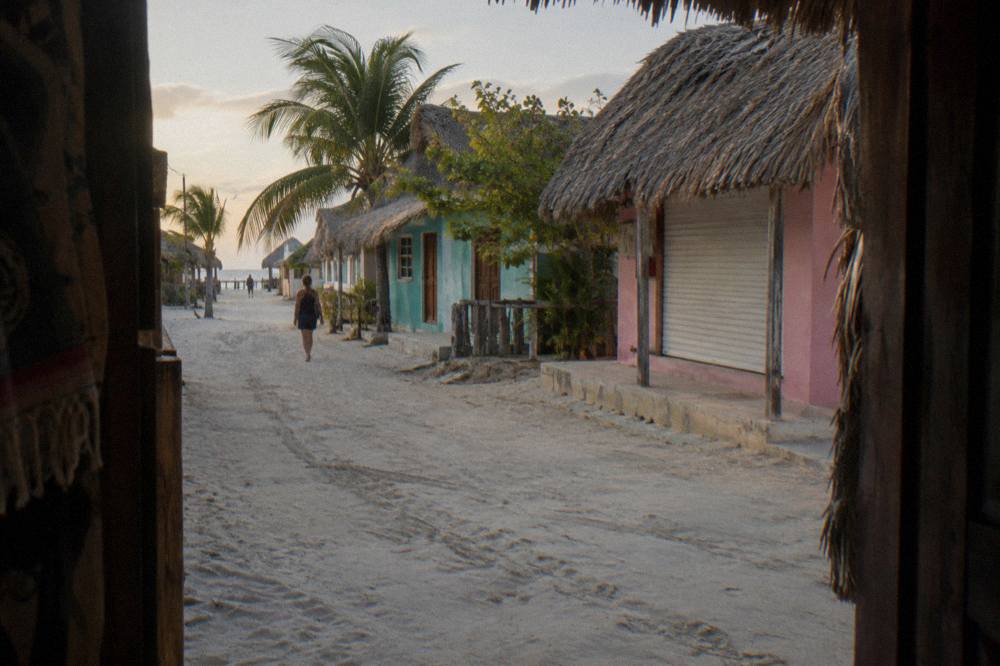 A quiet street of sand and colored storefronts on Holbox island in late afternoon light