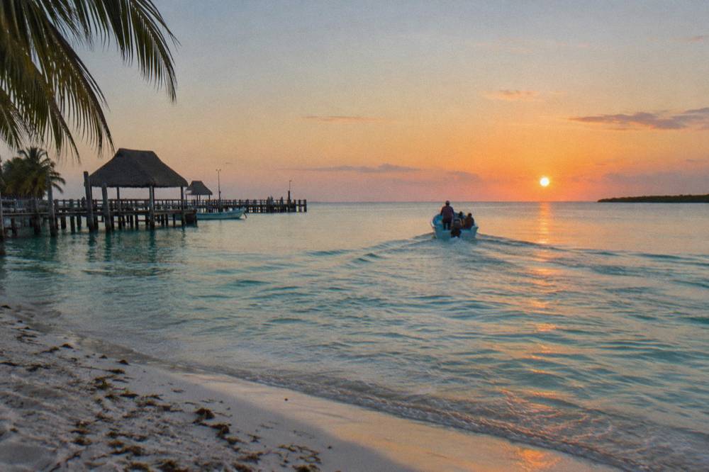 A small open boat heading out over calm turquoise water at sunrise near Holbox