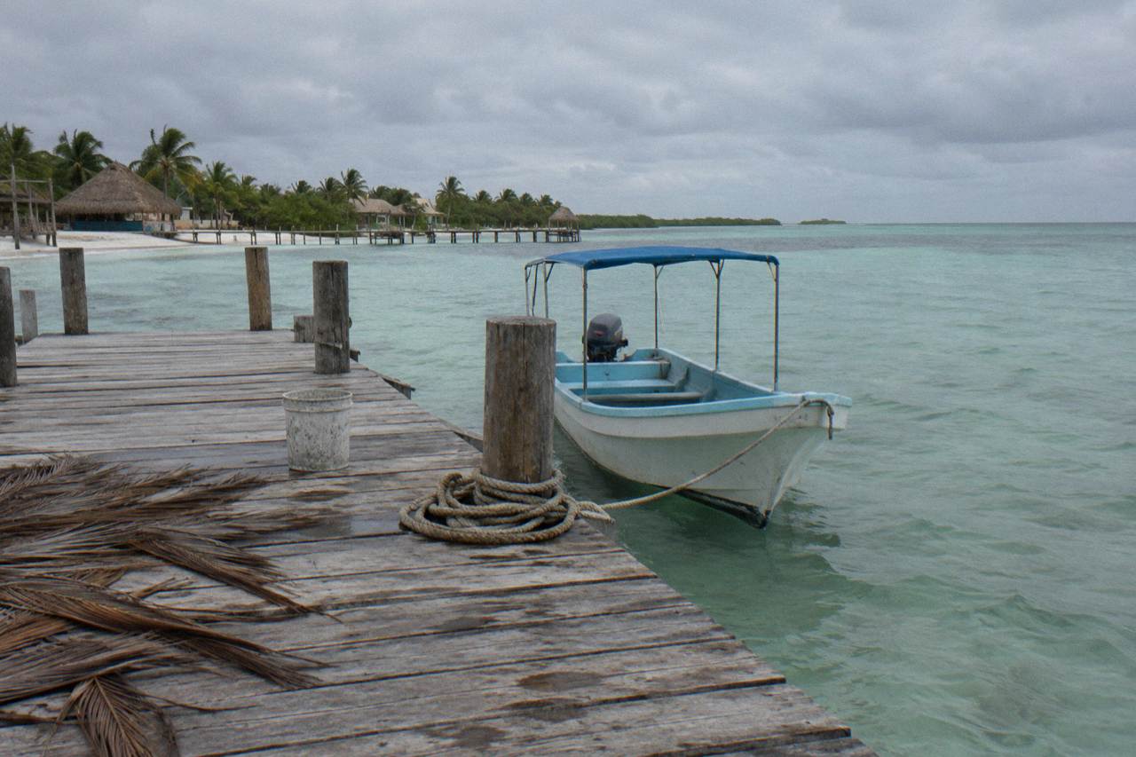 An empty wooden tour boat moored at a quiet Holbox dock under an overcast sky