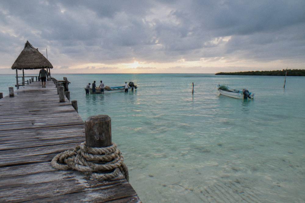 Wooden dock extending into clear shallow water at first light with clouds overhead