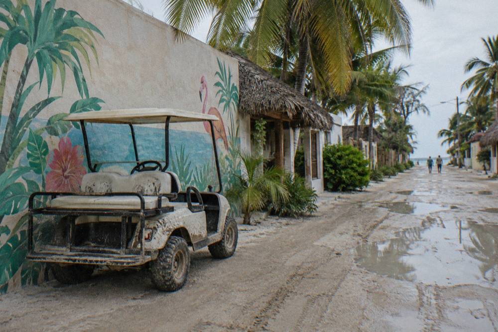 Golf cart parked on a sandy side street beside a wall painted with a colourful mural