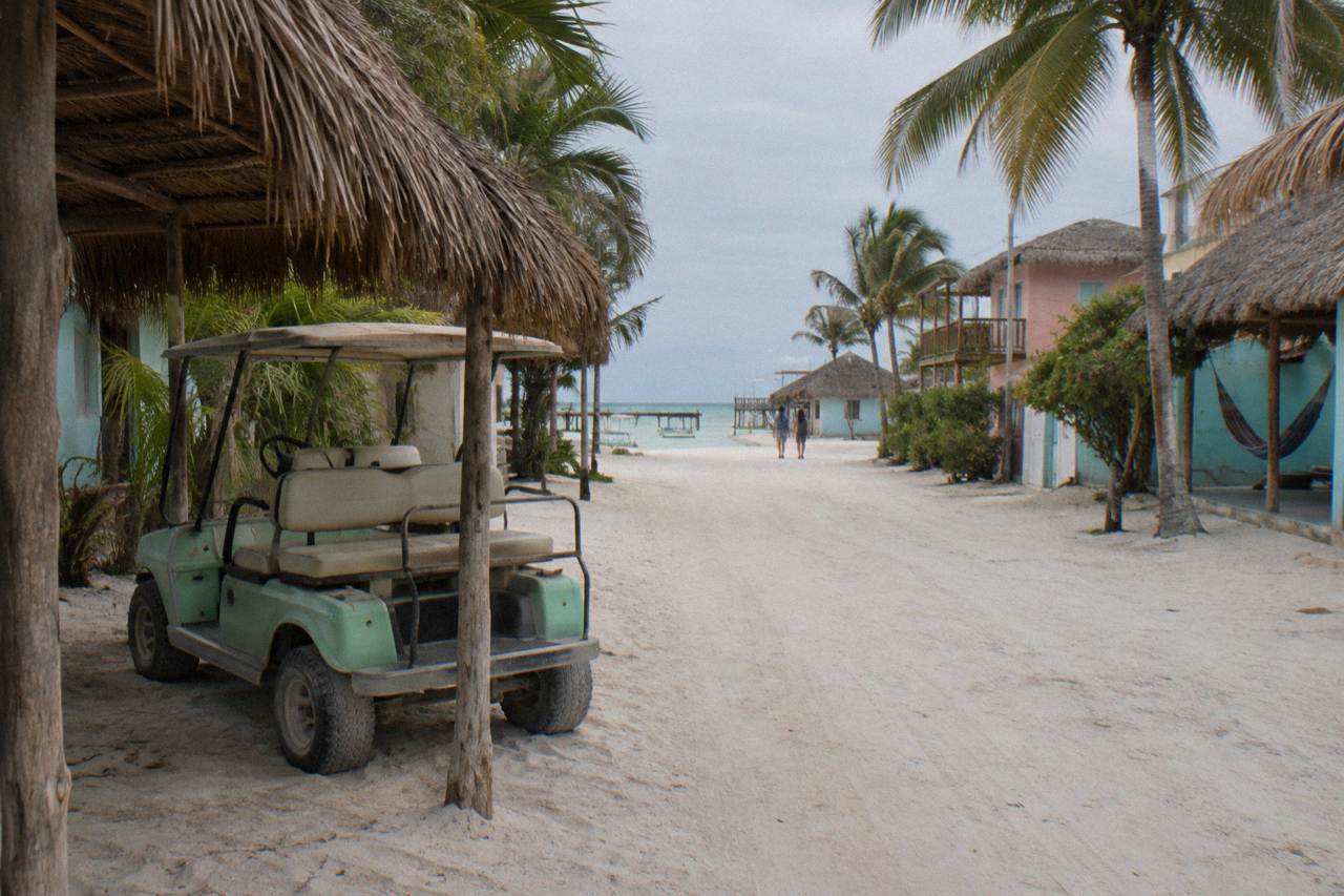 Empty sand street on Holbox with pastel painted buildings and a parked golf cart under a soft sky