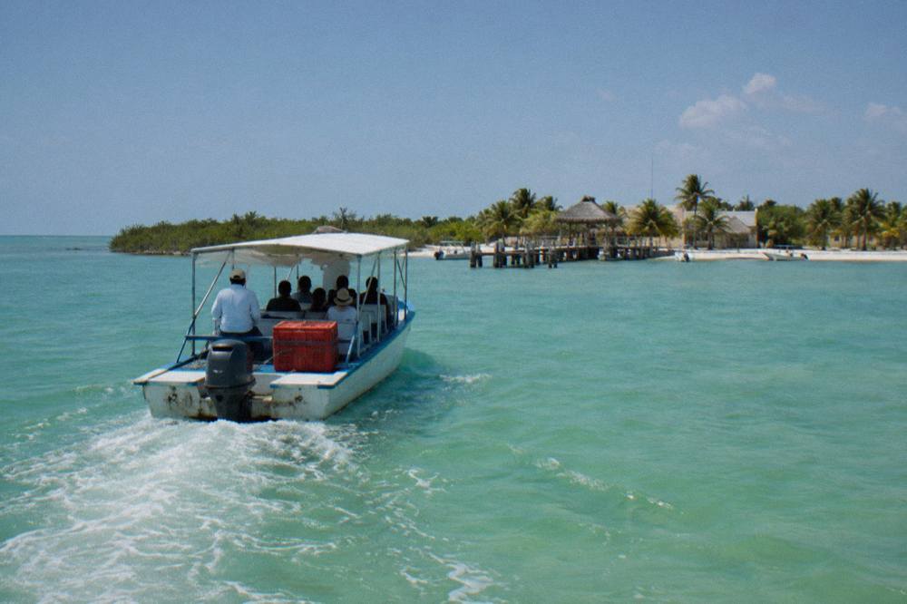 A small passenger ferry crossing a shallow turquoise lagoon toward an island dock