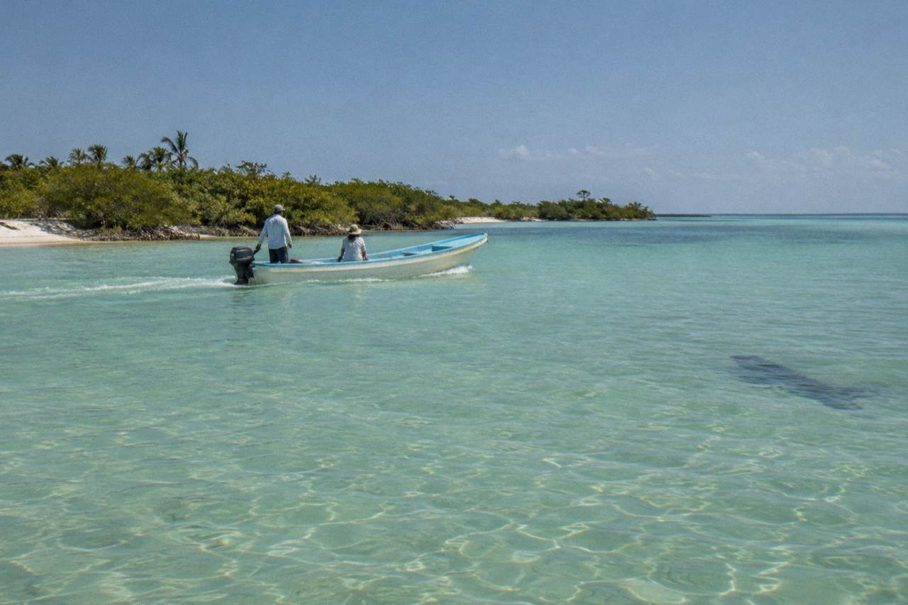 A small open boat crossing calm turquoise water off a sandy island shoreline