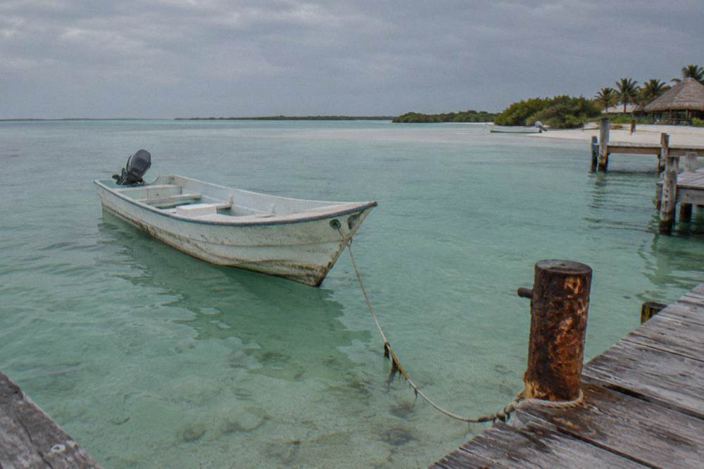 An empty wooden boat anchored over clear shallow water near a sandbank