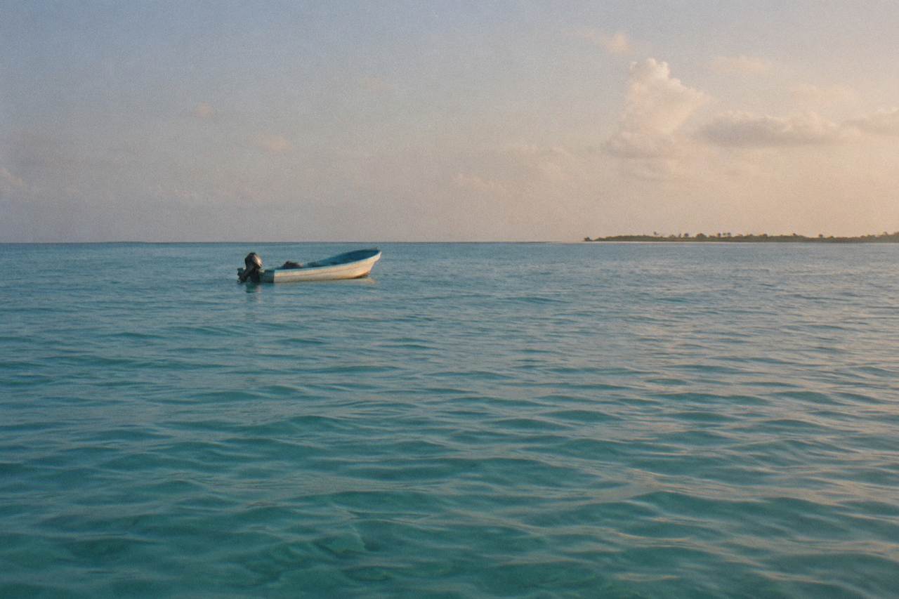Calm turquoise water off a tropical island with a small fishing boat on the horizon