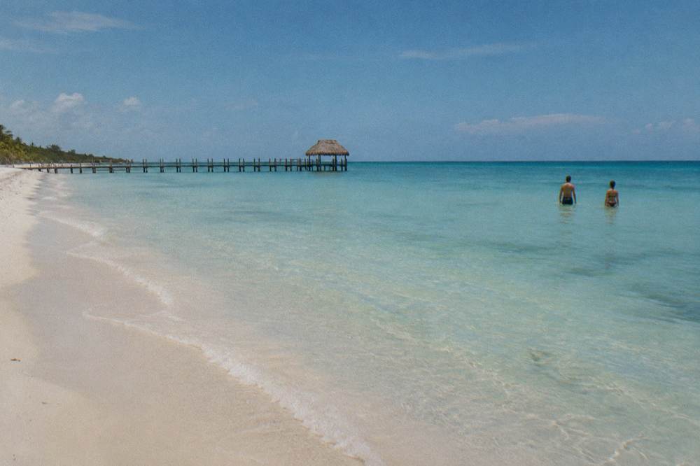 Calm shallow turquoise water along a wide empty sand beach at midday