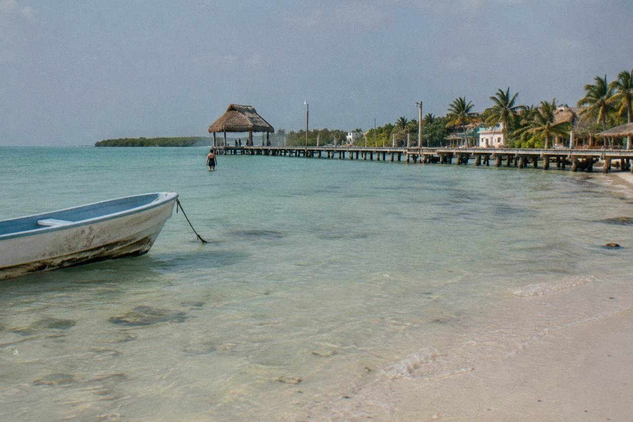 Calm shallow turquoise water along a sandy Holbox shoreline with a wooden dock in the distance