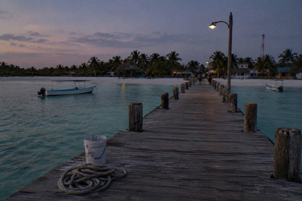 Wooden pier extending over calm green-blue shallow water at dusk