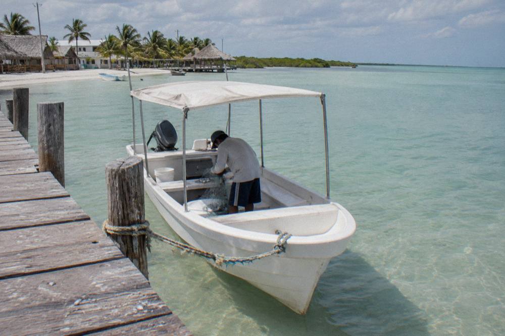 A small open fishing boat with a canvas roof moored at a wooden dock beside calm shallow water