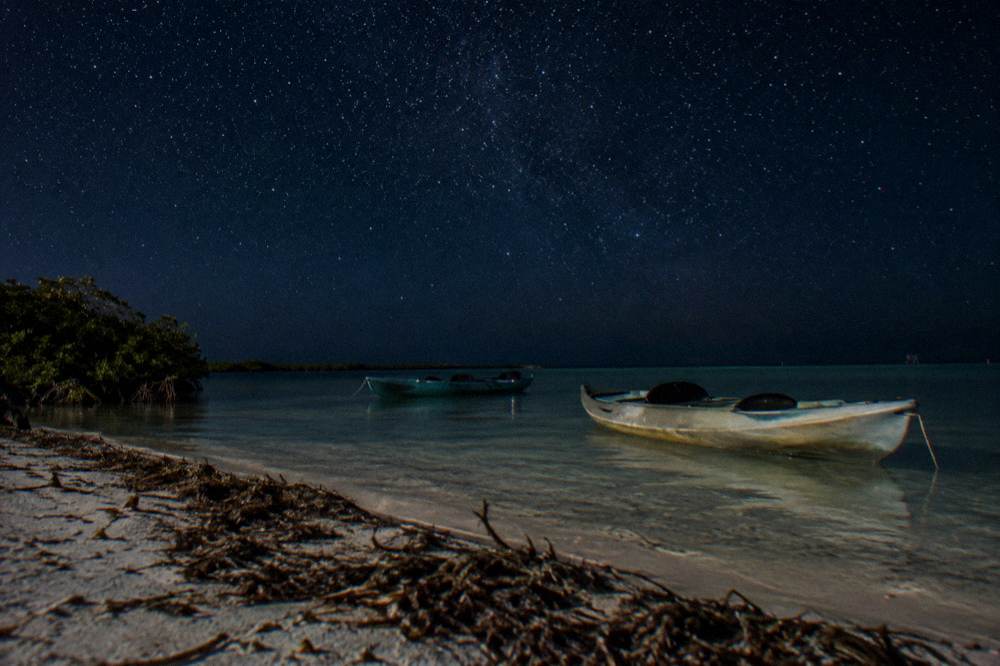 Two kayaks resting on dark calm water under a star-filled night sky