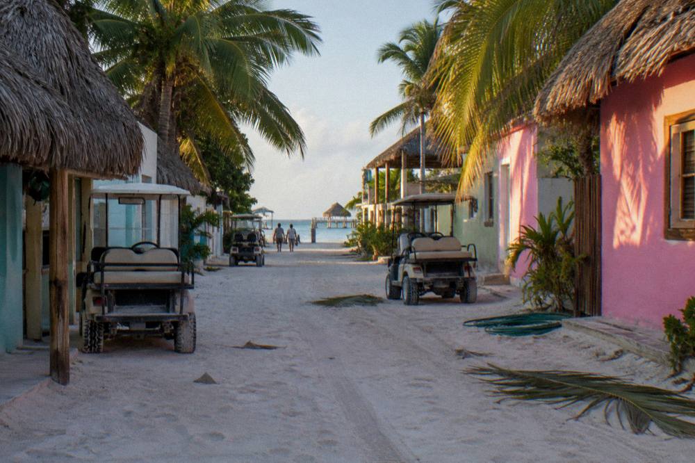 Sand street with golf carts parked beside pastel painted buildings on a car-free island