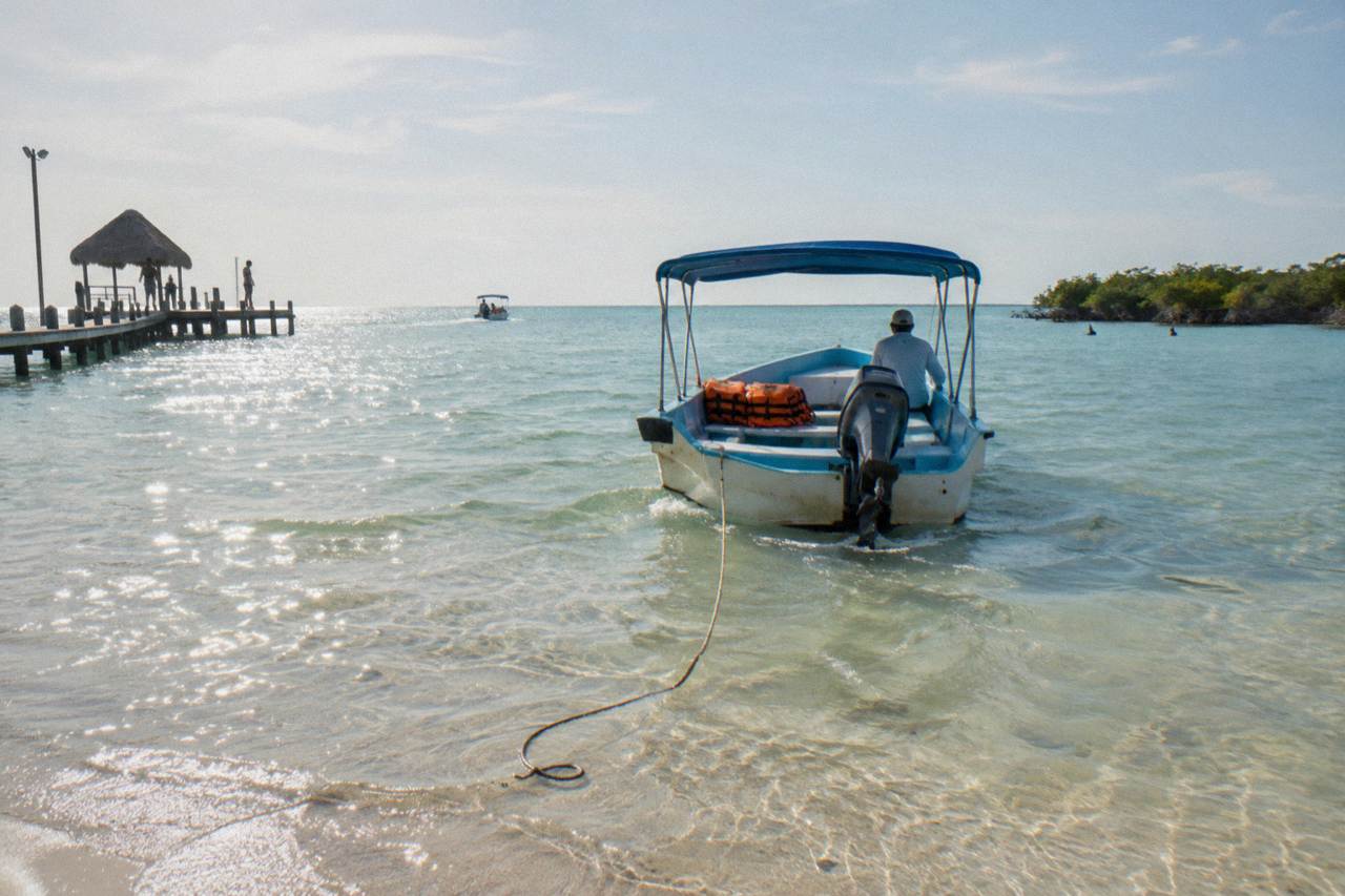 A small open boat on calm turquoise water near Holbox heading toward open sea
