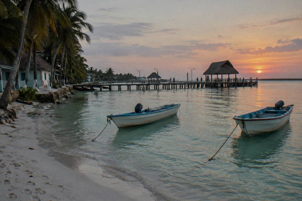 Wooden pier on Holbox with small fishing boats moored in shallow green water