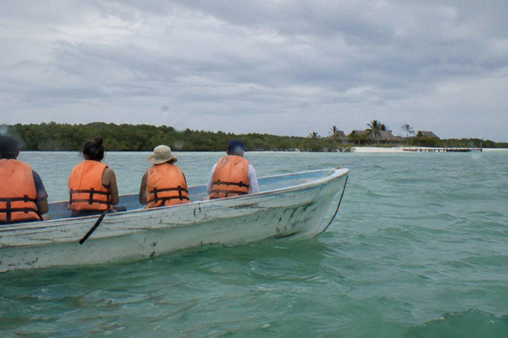 Travelers in life vests sitting along the gunwale of a small boat in open water