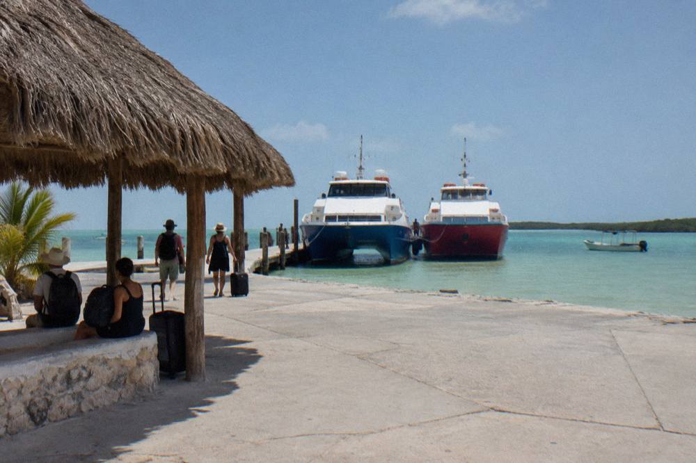 Blue and red ferry boats moored at the Chiquila dock with passengers waiting to board