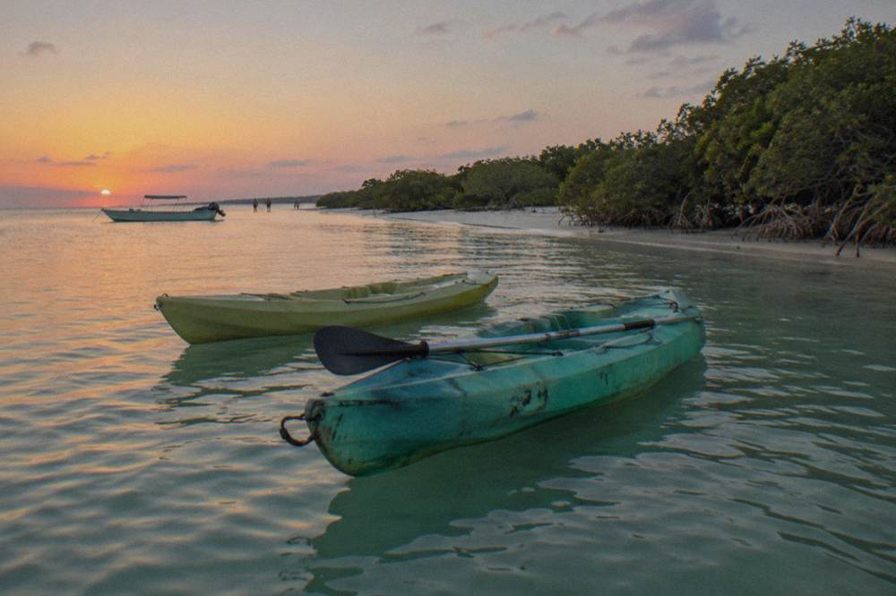 Two kayaks floating on calm dark water at dusk near the Holbox shoreline