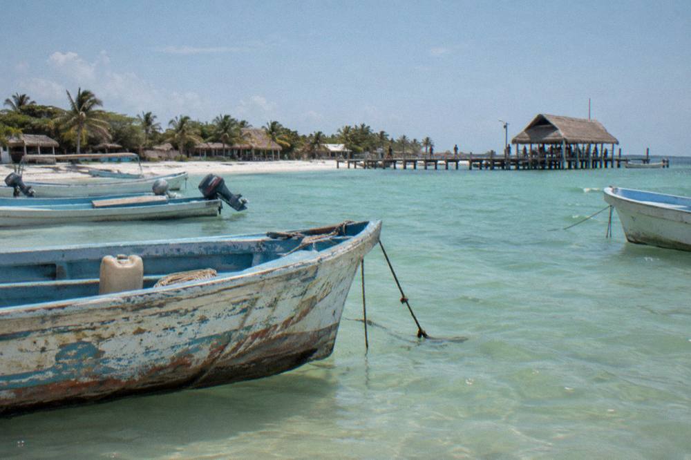Wooden fishing boats anchored in shallow green water beside a sandy spit near Holbox
