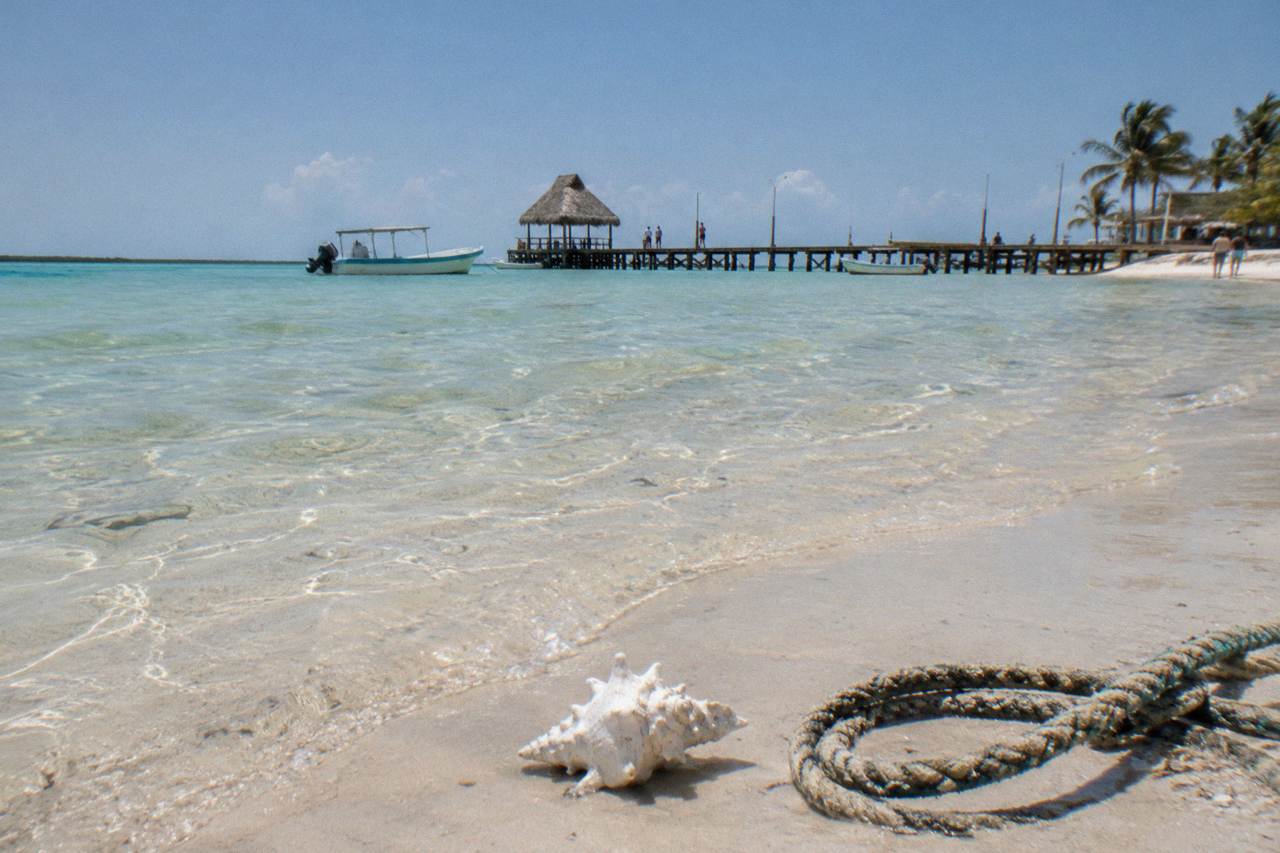 Calm shallow turquoise water along a sandy beach on Holbox with a wooden pier in the distance