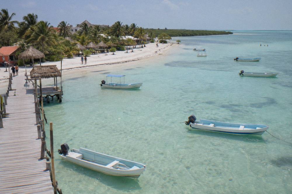Wooden boats resting in shallow turquoise water beside a sandy Holbox beach at midday
