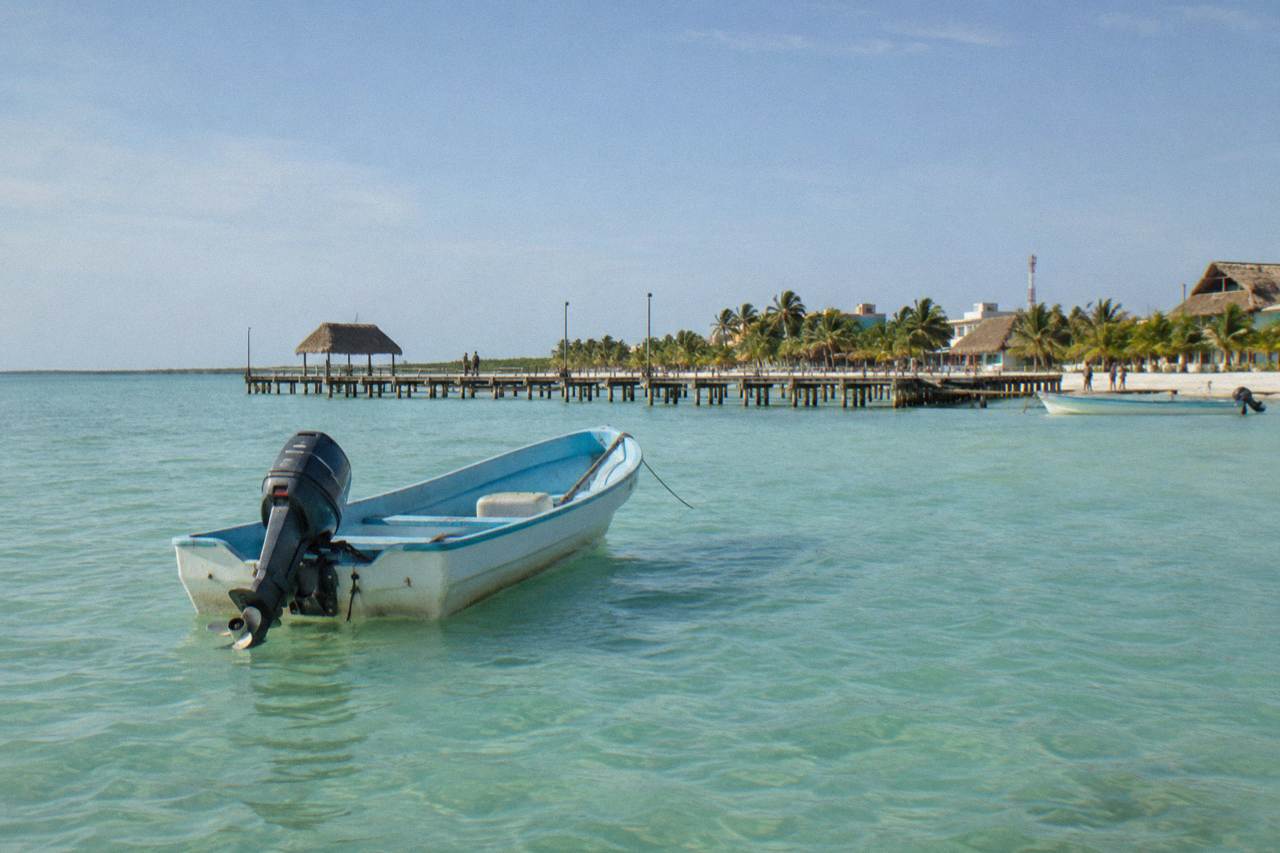 A small boat holding position in calm turquoise water near Holbox under a wide morning sky