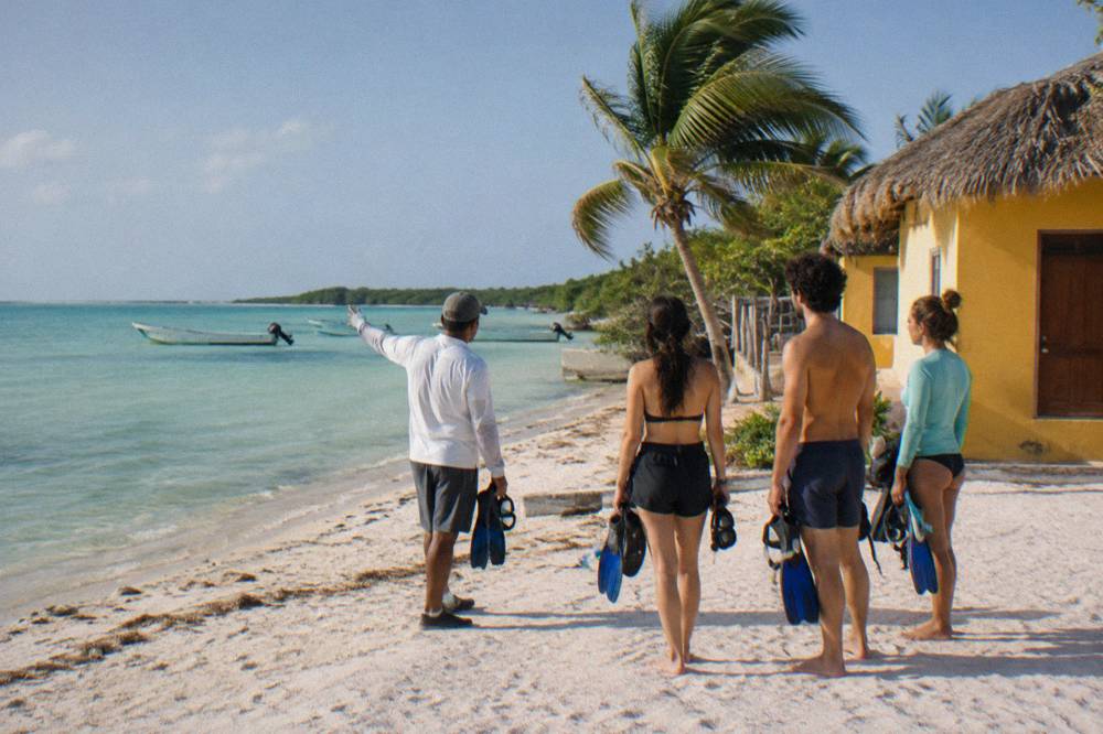 A guide speaking to a small group of snorkelers holding gear on a beach