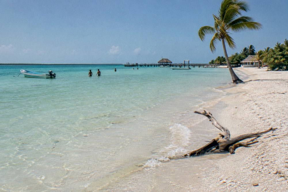 Wide empty beach with pale sand and calm shallow water under a clear morning sky