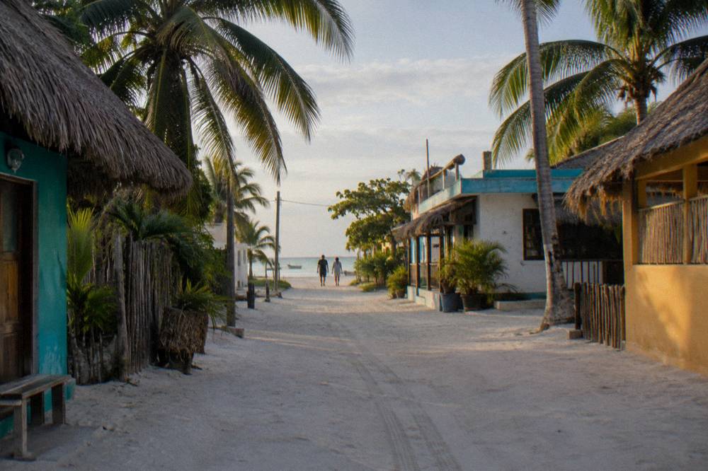 A quiet sandy street with palm trees and low colorful buildings in late afternoon light