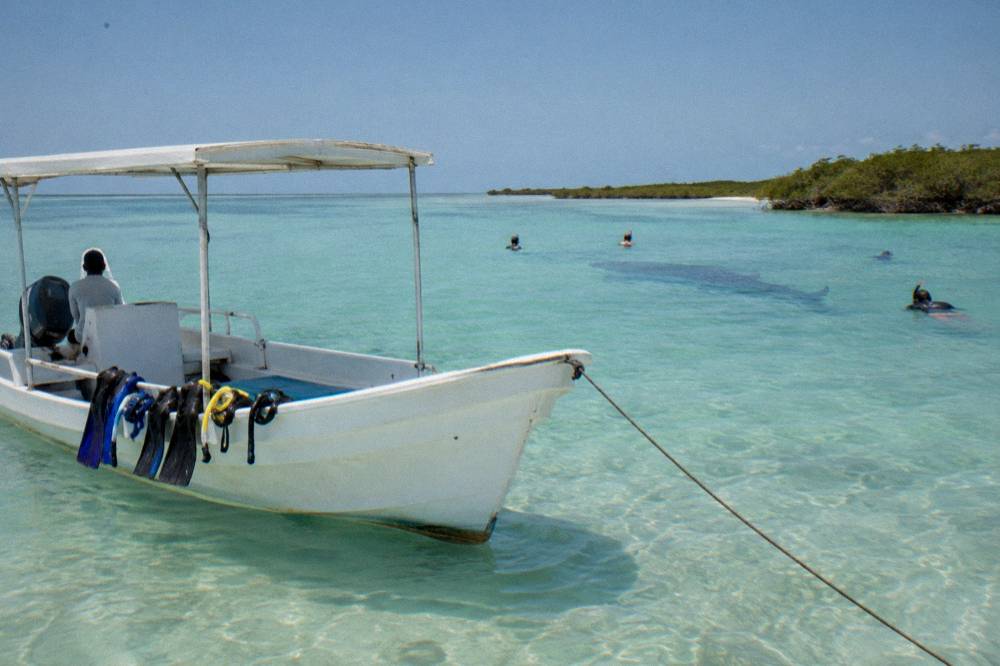 A white boat anchored over shallow turquoise water near a sandbar at midday