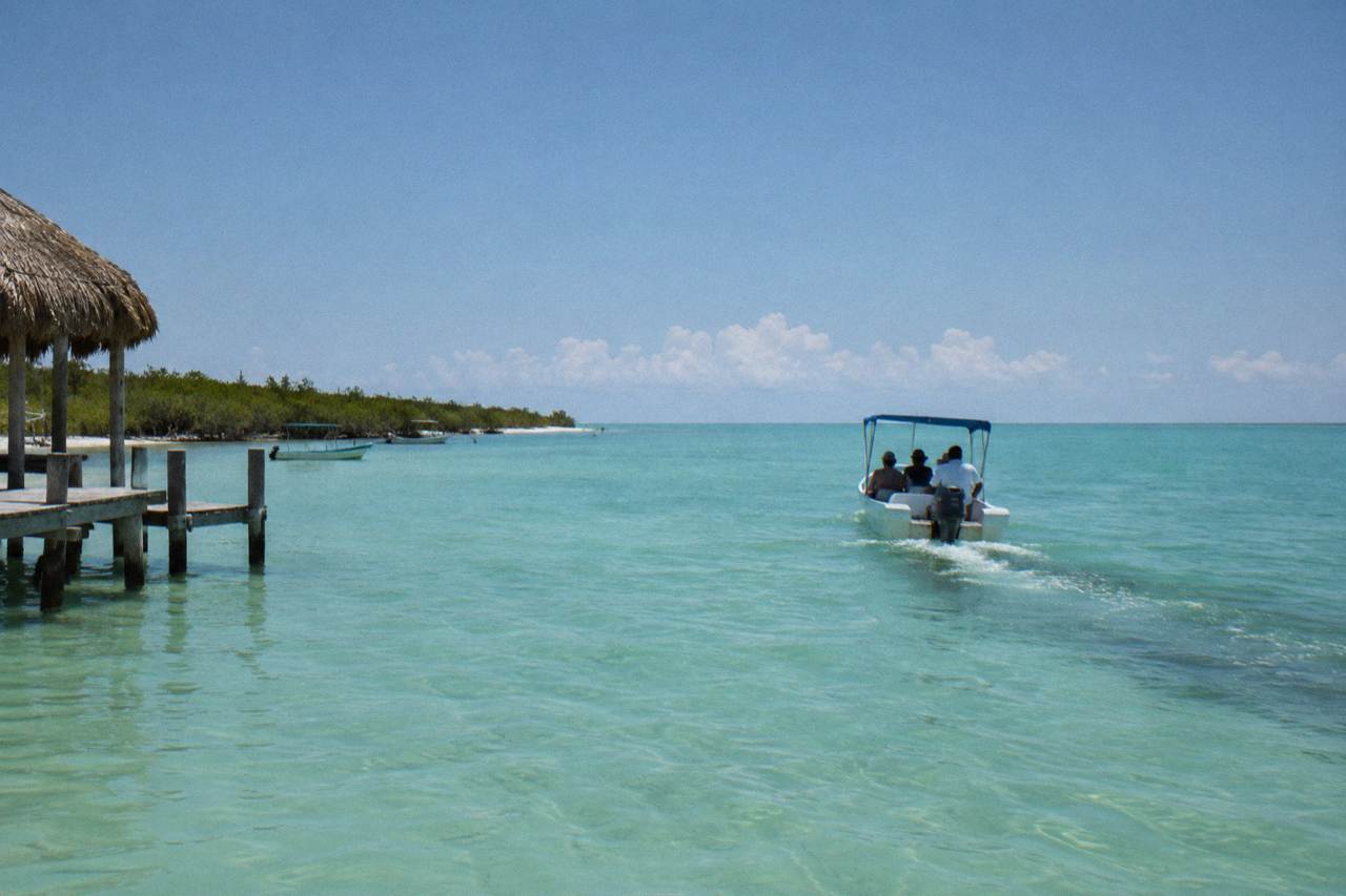 A small boat crossing open turquoise water near a line of white clouds on the horizon