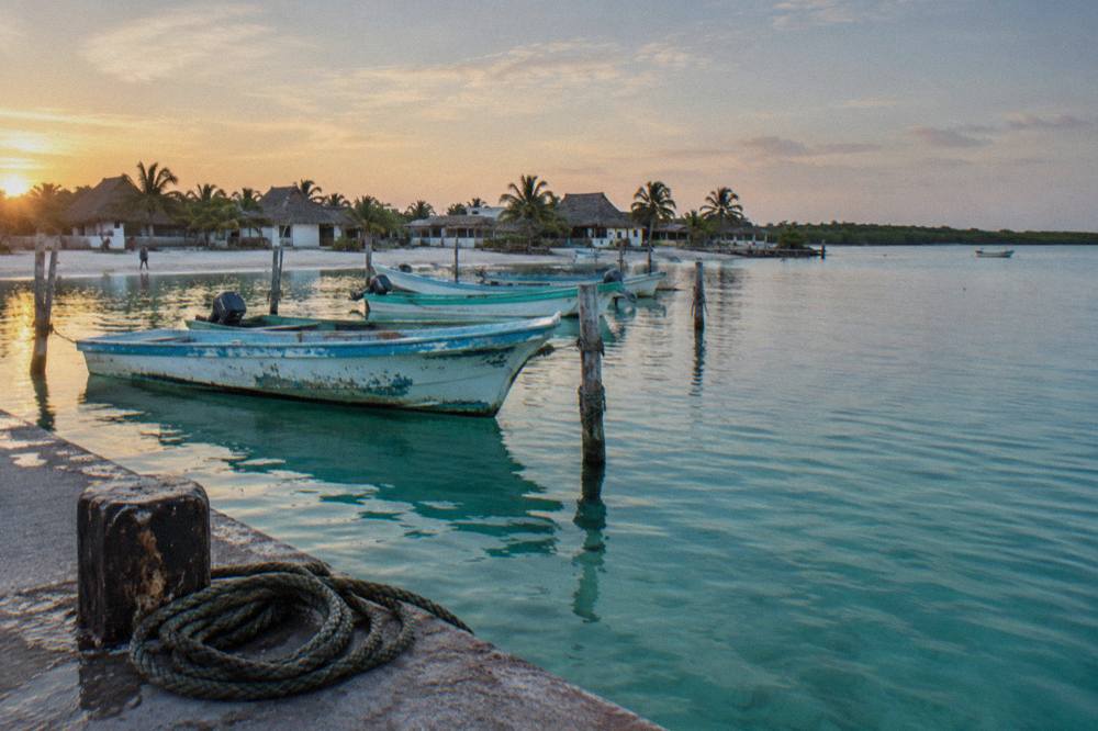 Wooden fishing boats moored at a small dock on a calm turquoise bay at dawn