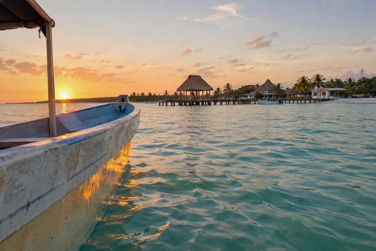 A small open boat crossing calm turquoise water off Holbox at sunrise