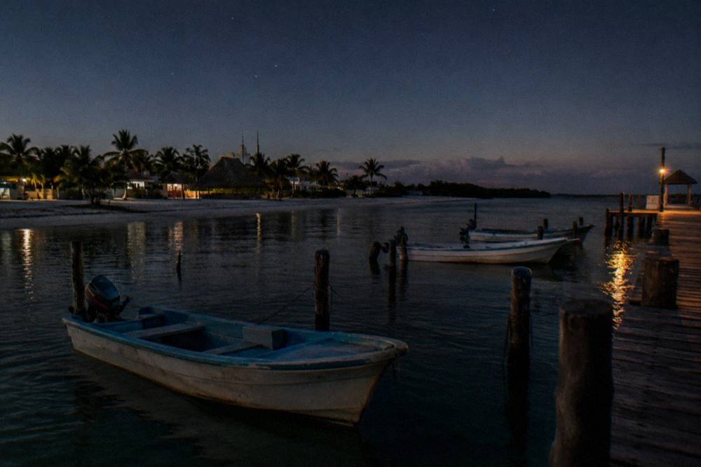 Wooden fishing boats moored at a dock on calm water before sunrise