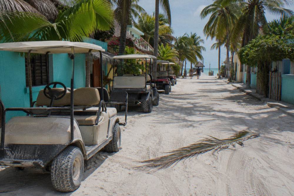 Golf carts parked on a sandy street beside palm trees in Holbox
