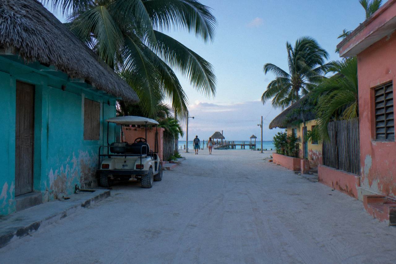 Quiet sandy street in Holbox village with colourful low buildings under a morning sky